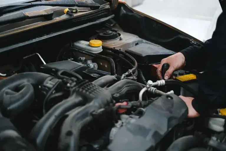 Hands working under the bonnet of a car during engine-bay maintenance