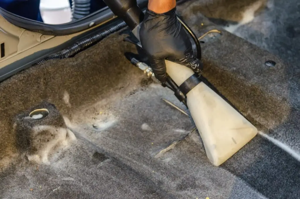 Gloved hand using an extraction nozzle to deep-clean a car carpet