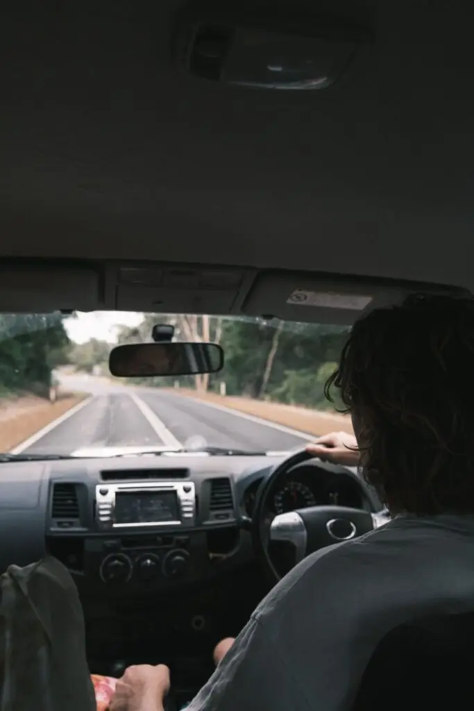 View from the rear seat of a car, showing the driver, dashboard and road through the windshield