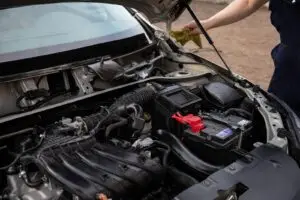 Open car hood showing the engine bay and battery, with a person beside the vehicle