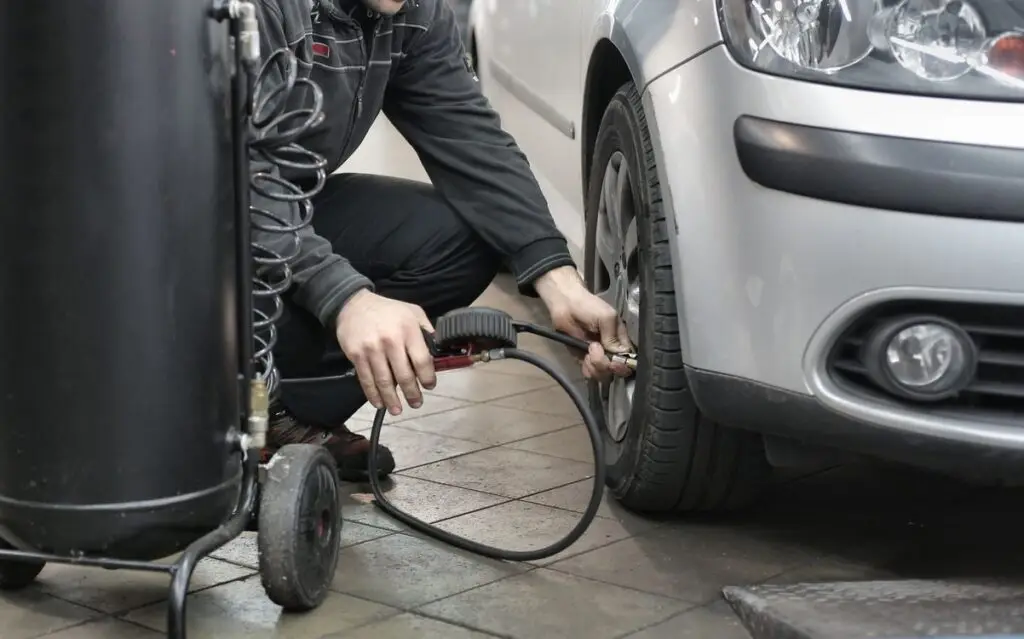 Mechanic using an air hose and pressure gauge beside a car tire in a workshop