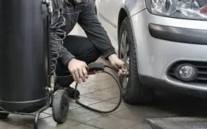 Mechanic using an air hose and pressure gauge beside a car tire in a workshop