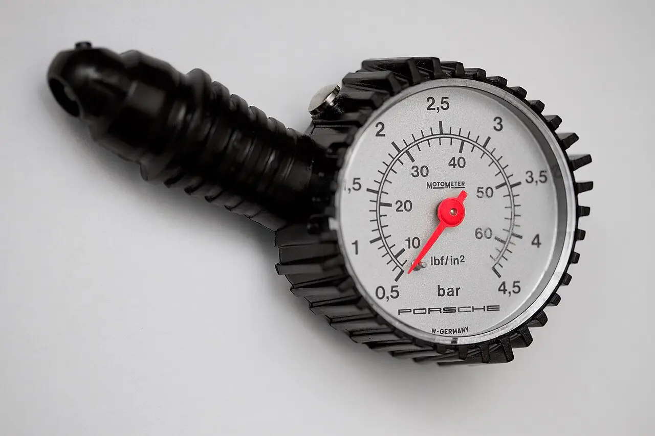 Close-up of a Porsche dial tire pressure gauge with bar and psi scales and a protective rubber cover.