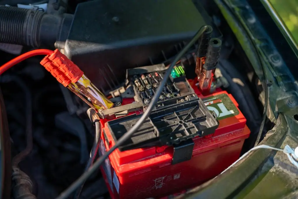 Close-up of a red car battery with red and black jumper clamps in the engine bay