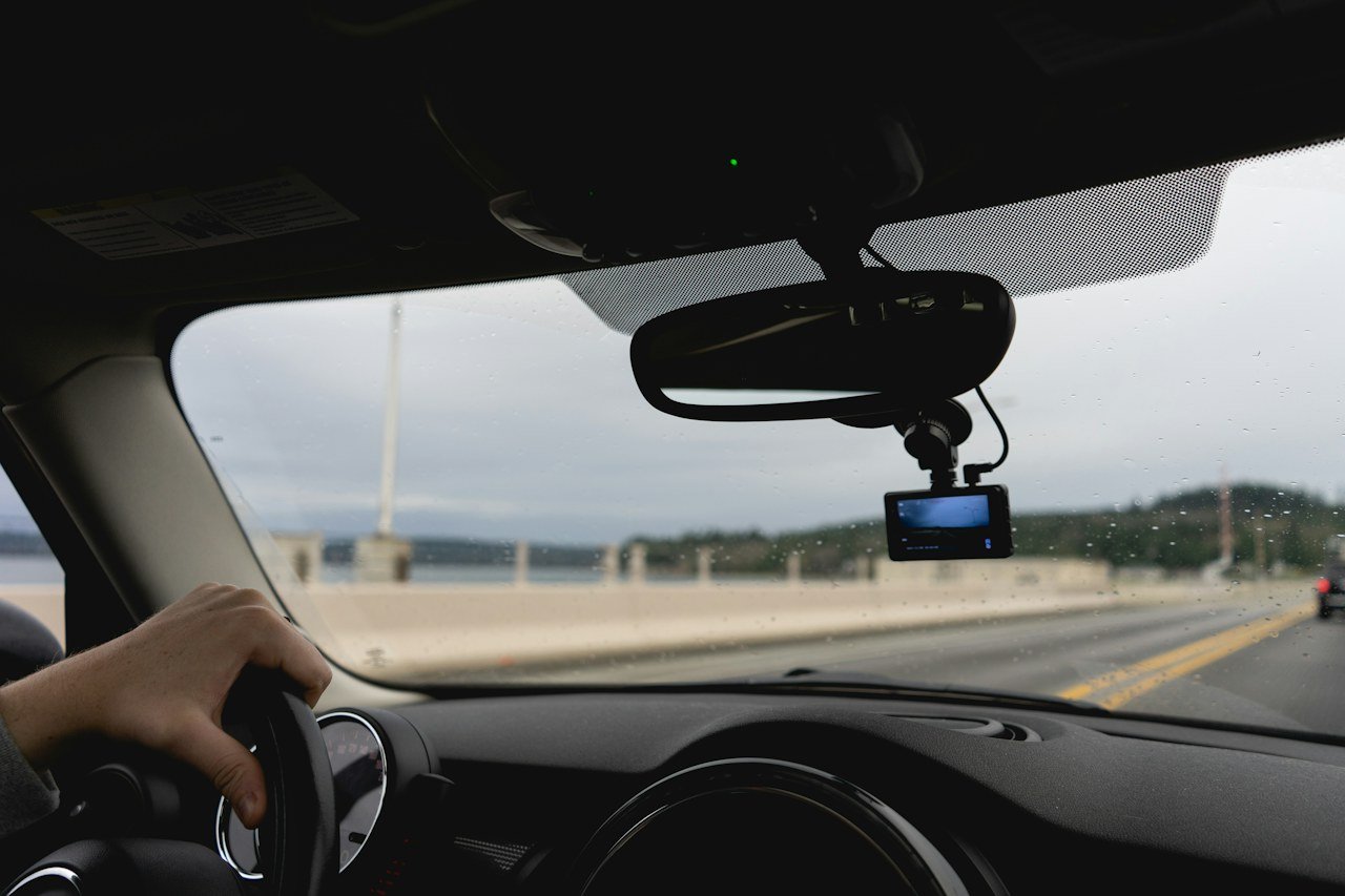 A dash camera mounted below a rear-view mirror during highway driving